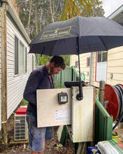 Load image into Gallery viewer, The Trade Shade - Magnetic Umbrella Holder Keeping An Electrician Dry While He Carries Out Repairs On A Switchboard.
