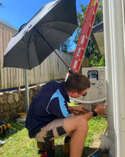 Load image into Gallery viewer, The Trade Shade - The Square Umbrella Shading An Australian Outdoor Worker Diagnosing An Air-Conditioner.
